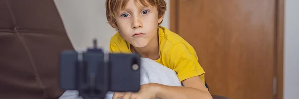 BANNER, LONGO FORMATO Manter-me ligado. Menino feliz olhando para seu telefone celular e sorrindo enquanto brincava com brinquedos. Um menino fala com alguém através de comunicação de vídeo durante o auto-isolamento devido a — Fotografia de Stock