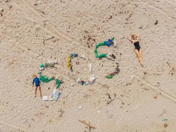 SOS-Schriftzug und Mutter und Sohn sonnen sich am Strand in der Nähe. Umweltproblem. Ökologiekonzept. Plastik am Strand mit einem Schriftzug. Verschütteter Müll am Strand — Stockfoto