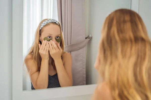 镜像反射微笑的女人应用水凝胶眼科护理补丁，眼部皮肤保湿，享受护肤程序 — 图库照片