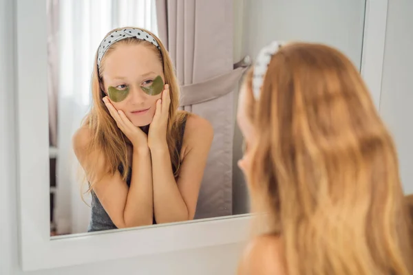 Зеркальное отражение улыбающаяся женщина, использующая гидрогель для ухода за глазами, увлажняющая кожу под глазами, наслаждающаяся процедурами по уходу за кожей — стоковое фото