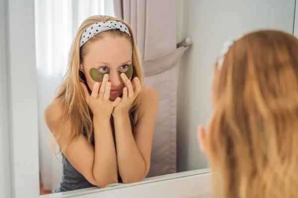 Riflessione a specchio donna sorridente che applica patch per la cura degli occhi idrogel, idratando la pelle sotto gli occhi, godendo di procedure di cura della pelle — Foto Stock