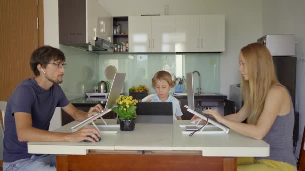 Eine junge Frau und ein Mann arbeiten in ihrem Wohnzimmer, die Küche im Hintergrund. Ihr Sohn lernt online mit einem Tablet. Beide müssen aufgrund der Covid-19-Beschränkungen aus der Ferne arbeiten — Stockvideo