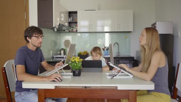 Seorang wanita muda dan pria bekerja di ruang tamu mereka dengan dapur di latar belakang. Anak mereka belajar online menggunakan tablet. Keduanya harus bekerja jauh karena pembatasan Kovid-19 — Stok Video