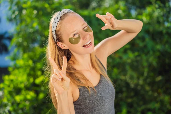 Smiling woman applying hydrogel eye care patches, moisturizing skin under eyes, enjoying skincare procedures — Stock Photo, Image