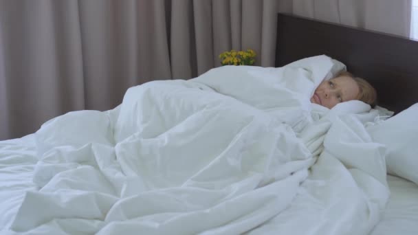 Młoda kobieta marznie w łóżku. Próbuje się rozgrzać pod kocem. Gorączka. Koncepcja zimnej pogody. — Wideo stockowe