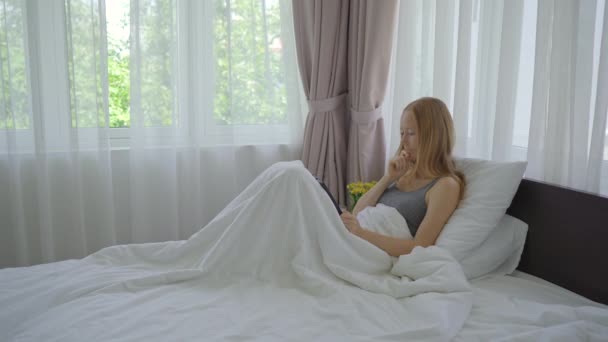 ベッドに寝そべっている若い女性がビデオ会議を通して誰かと話をする。COVID社会的距離。新しい正常よ。接続されたコンセプトを維持 — ストック動画