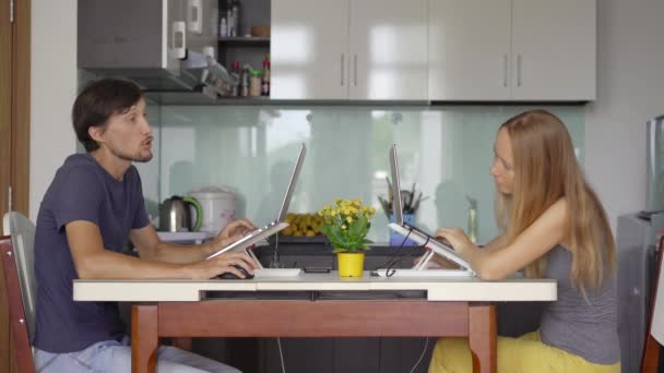 En ung kvinna och man arbetar i sitt vardagsrum med köket i bakgrunden. Båda måste arbeta på distans på grund av restriktionerna i Covid-19. Han spelar dataspel. — Stockvideo
