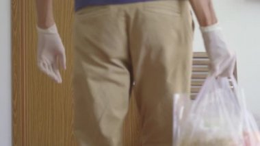 Gönüllü bir adam, kendini karantinaya almış biri için yemek dağıtıyor. Kapı kolunda karantina işareti var. Ev kavramında karantina. Tecrit edilmiş insanlar için yemek teslimatı. COVID-19 kavramı