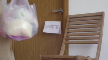 Gönüllü bir adam, kendini karantinaya almış biri için yemek dağıtıyor. Kapı kolunda karantina işareti var. Ev kavramında karantina. Tecrit edilmiş insanlar için yemek teslimatı. COVID-19 kavramı