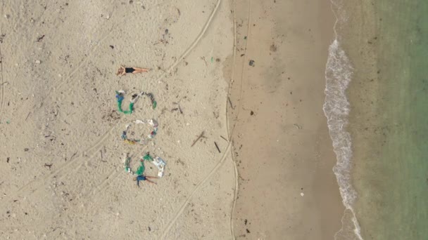 Vertikales Video. Luftaufnahme des Schildes SOS aus Müll an einem Strand. Frau legt sich neben das Schild, das sie unterstreicht. Ökologisches Katastrophenkonzept. Konzept zur Plastikverschmutzung — Stockvideo