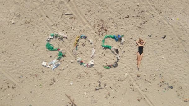 Αεροφωτογραφία της πινακίδας SOS φτιαγμένη από σκουπίδια σε μια παραλία. Η γυναίκα ξαπλώνει δίπλα στο ζώδιο σιγοβράζοντας ένα θαυμαστικό. Οικολογική έννοια καταστροφής. Έννοια πλαστικής ρύπανσης — Αρχείο Βίντεο