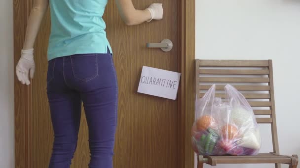 A woman volunteer delivers food for a person locked down in a self-quarantine. A sign Quarantine on the door handle. Quarantining at home concept. Food delivery for isolated people. COVID-19 concept — Stock Video