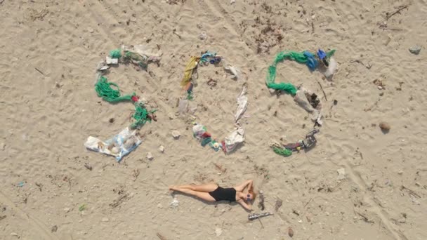 Foto udara dari tanda SOS yang terbuat dari sampah di pantai. Wanita berbaring dengan tanda menggarisbawahi itu. Konsep bencana ekologi. Konsep polusi plastik — Stok Video