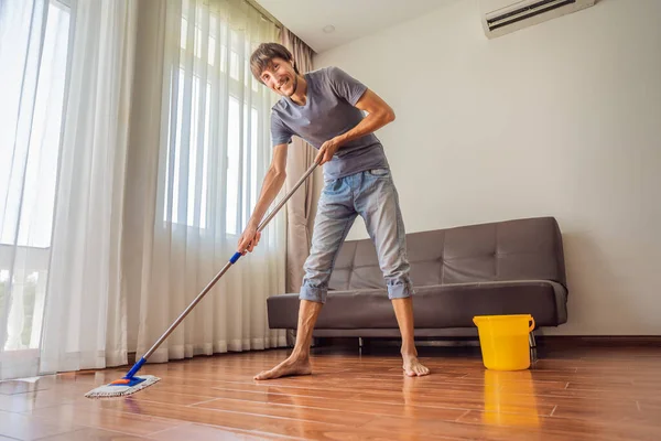 Young man with mop cleaning floor at home