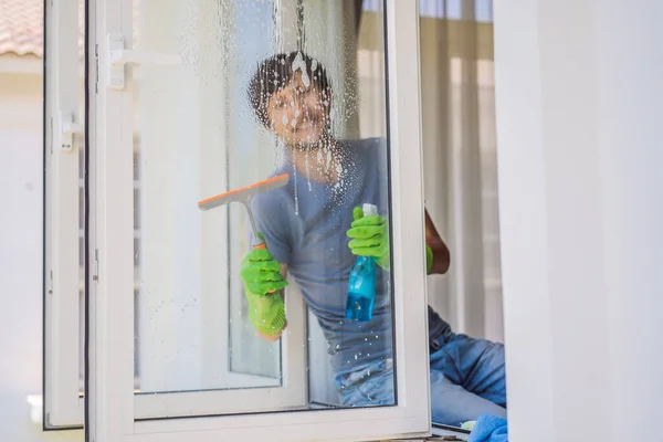 Un joven limpiando la ventana con un limpiacristales — Foto de Stock