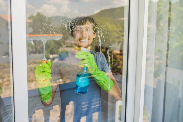 Un joven limpiando la ventana con un limpiacristales — Foto de Stock