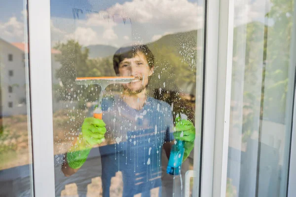 Um jovem limpando a janela com um limpador de janelas — Fotografia de Stock