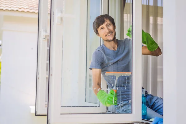 Ein junger Mann putzt das Fenster mit einem Fensterputzer — Stockfoto