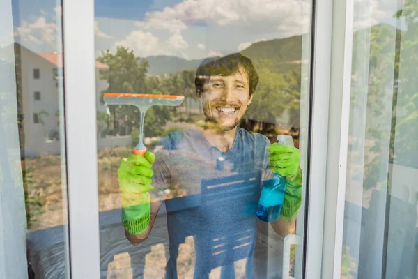 Un joven limpiando la ventana con un limpiacristales — Foto de Stock