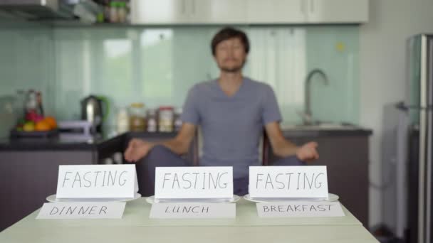 A young man meditates in frint of a table with empty plates on which writtings " fasting" are placed. Yoga diet. Interval fasting concept. Skipping meals — Stock Video