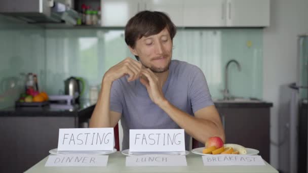 Mutlu genç bir adam sağlıklı bir kahvaltı ederken işaretler boş tabaklar üzerinde öğle ve akşam yemeklerini gösteriyor. Perhiz konsepti. Öğün atlama — Stok video