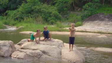 Küçük bir nehrin ortasındaki bir kayanın üzerinde oynayan bir grup çocuk. Arkadaşlık kavramı. Arkadaşlarla yaz.