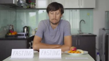 Üzgün genç bir adam boş tabaklar üzerine işaretler koyar öğle ve akşam yemekleri ve sonra kahvaltı tabağından bir elma yer. Perhiz konsepti. Öğün atlama