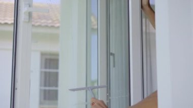 Genç bir adam cam temizleme sıvısı kullanarak pencereleri yıkıyor. Temizlik hizmeti kavramı