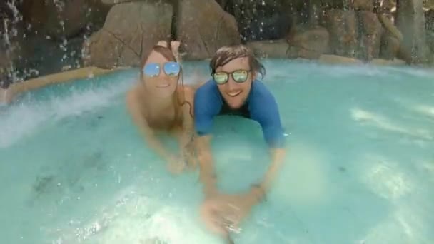 Ein junges Paar macht fröhliche Ferien in einem Wasserresort. Sie lagen unter einem künstlichen Wasserfall in einem Kurzentrum — Stockvideo