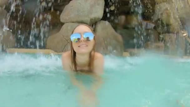 Een gelukkige jonge vrouw ligt onder een kunstmatige waterval in een kuuroord — Stockvideo