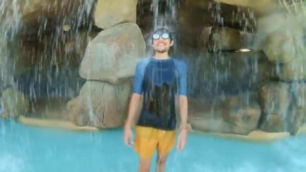 Egy boldog fiatalember áll egy mesterséges vízesés alatt egy spa központban. — Stock videók