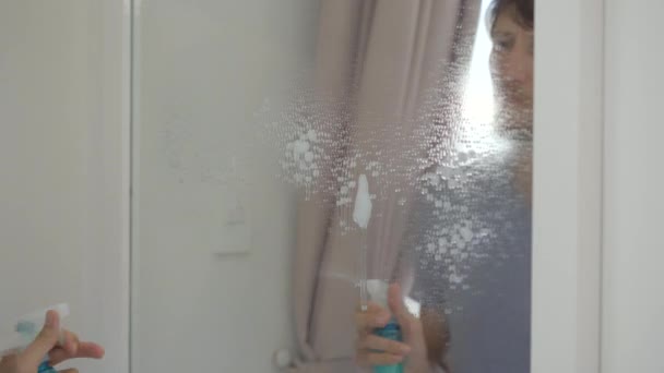 ガラスの掃除液で鏡を洗う青年。清掃サービスのコンセプト。男女共同参画の概念 — ストック動画