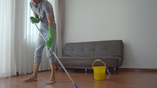 Un joven con guantes de goma verde lava el suelo en un apartamento. Servicio de limpieza concepto. Concepto de igualdad de género. — Vídeos de Stock