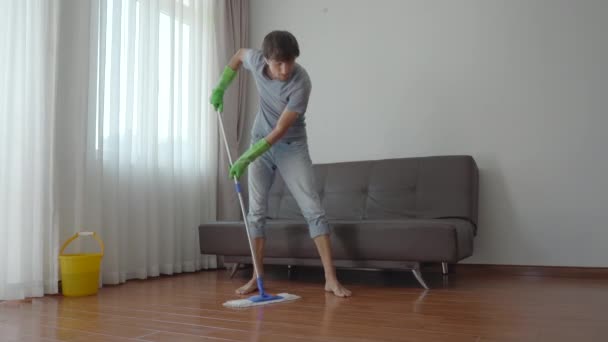 Un joven con guantes de goma verde lava el suelo en un apartamento. Servicio de limpieza concepto. Concepto de igualdad de género. — Vídeos de Stock