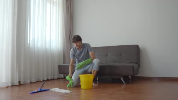 Un jeune homme en gants de caoutchouc vert lave le sol dans un appartement. Concept de service de nettoyage. Concept d'égalité des sexes. — Video