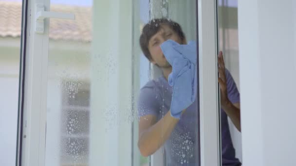 En ung man tvättar fönster med en glasrengöringsvätska. Begreppet städning — Stockvideo