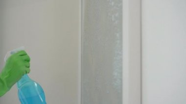 Lastik eldivenli genç bir adam aynayı cam temizleme sıvısıyla yıkıyor. Temizlik hizmeti konsepti. Cinsiyet eşitliği kavramı