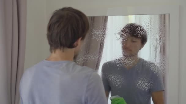 Mladý muž v gumových rukavicích myje zrcadlo čisticí kapalinou. Koncept úklidové služby. Koncept rovnosti pohlaví — Stock video