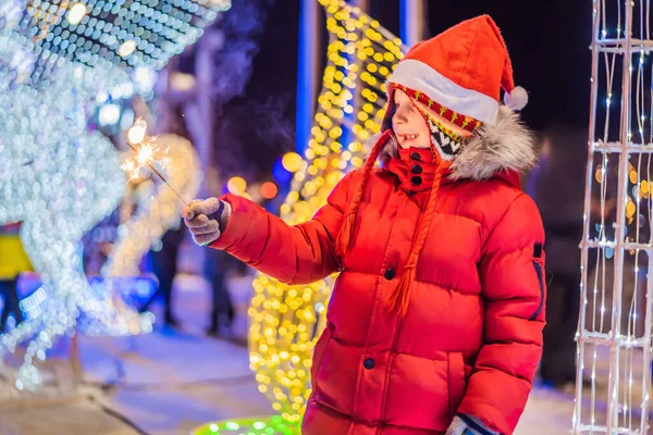 Kleine jongen met sterretjes in de buurt van grote dennenboom en kerstverlichting op de kerstmarkt. Kerstvakantie op kermis — Stockfoto