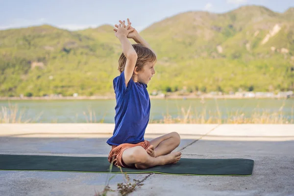 Мальчик, занимающийся йогой на коврике для йоги на фоне гор — стоковое фото