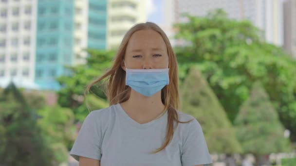 Una joven está parada en una calle. Ella está usando mascarilla médica de la manera equivocada. Su máscara no cubre su nariz. Manera incorrecta de usar una máscara facial — Vídeo de stock