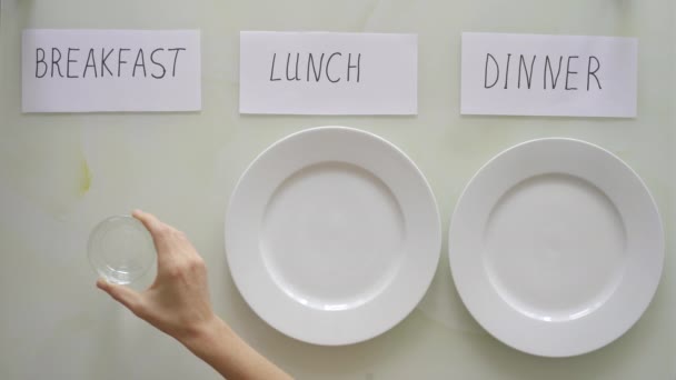 Kobieta zastępuje talerze pod tytułami śniadania, lunchu i kolacji szklankami z wodą. Koncepcja postu interwałowego. Omijanie posiłków — Wideo stockowe