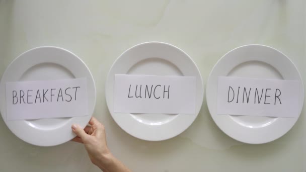 Una mujer reemplaza las inscripciones desayuno, almuerzo y cena en platos con inscripciones ayuno. Concepto de ayuno de intervalo. Saltarse las comidas — Vídeo de stock