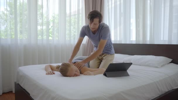 Um jovem casal no quarto. Homem aprende a realizar uma massagem corporal para uma mulher, assistindo a um vídeo de educação on-line em um tablet. Conceito de educação online. Eles ficam em casa por causa dos Covid. — Vídeo de Stock