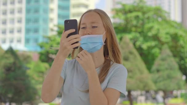 En una calle, una mujer joven habla con un teléfono que lleva máscara facial médica de la manera equivocada. Su máscara no cubre su nariz. Manera incorrecta de usar una máscara facial — Vídeo de stock