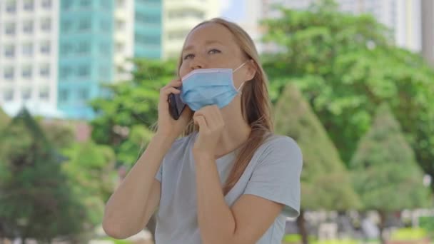 거리에서 한 젊은 여자가 의료용 마스크를 잘못 쓰고 있는 전화로 이야기를 합니다. 그녀의 마스크는 코를 가리지 않는다. 안면 마스크를 잘못 쓰는 방법 — 비디오