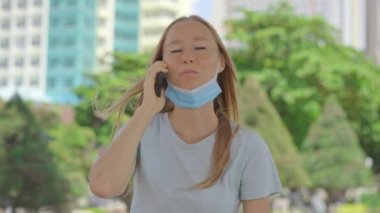 Sokakta genç bir kadın telefonla konuşuyor. Yüzünde tıbbi maske var. Maskesi yüzünü kapatmıyor. Yüz maskesi kullanmanın yanlış yolu.