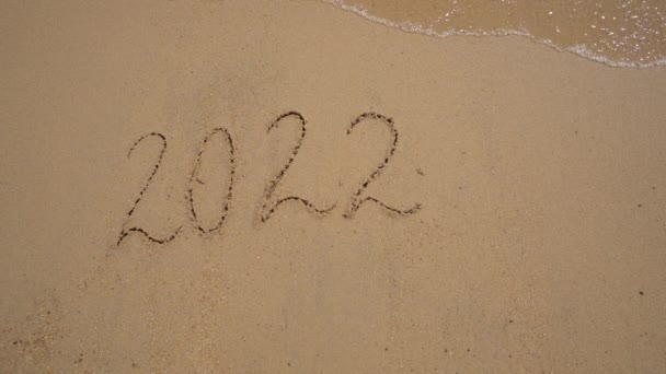 スローモーション撮影。砂の上に2022年の文字が海によって洗い流されています。人生の変化の概念。時代の変化 — ストック動画