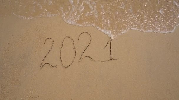 スローモーション撮影。砂の上に2021年の文字が海によって洗い流されています。人生の変化の概念。時代の変化 — ストック動画