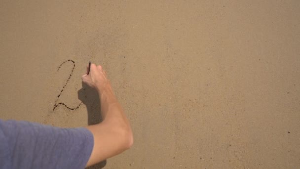 スローモーション撮影。男はビーチで砂の上に2022を書いています。人生の変化の概念。時代の変化 — ストック動画
